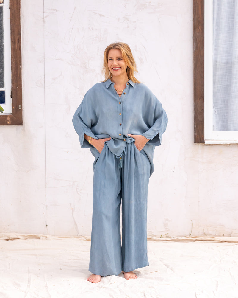 woman dressed in bouviet oversized shirt and miguel straight legged pants in orange peel fibre in cornflower blue standing in front of a white wall