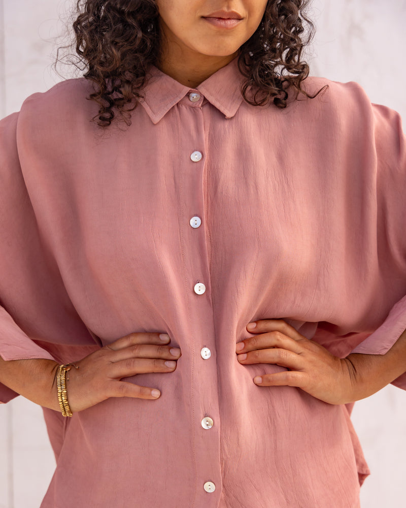 
                  
                    woman dressed in bouviet oversized shirt and miguel straight legged pants in orange peel fibre in dirty rose pink standing in front of a white wall
                  
                