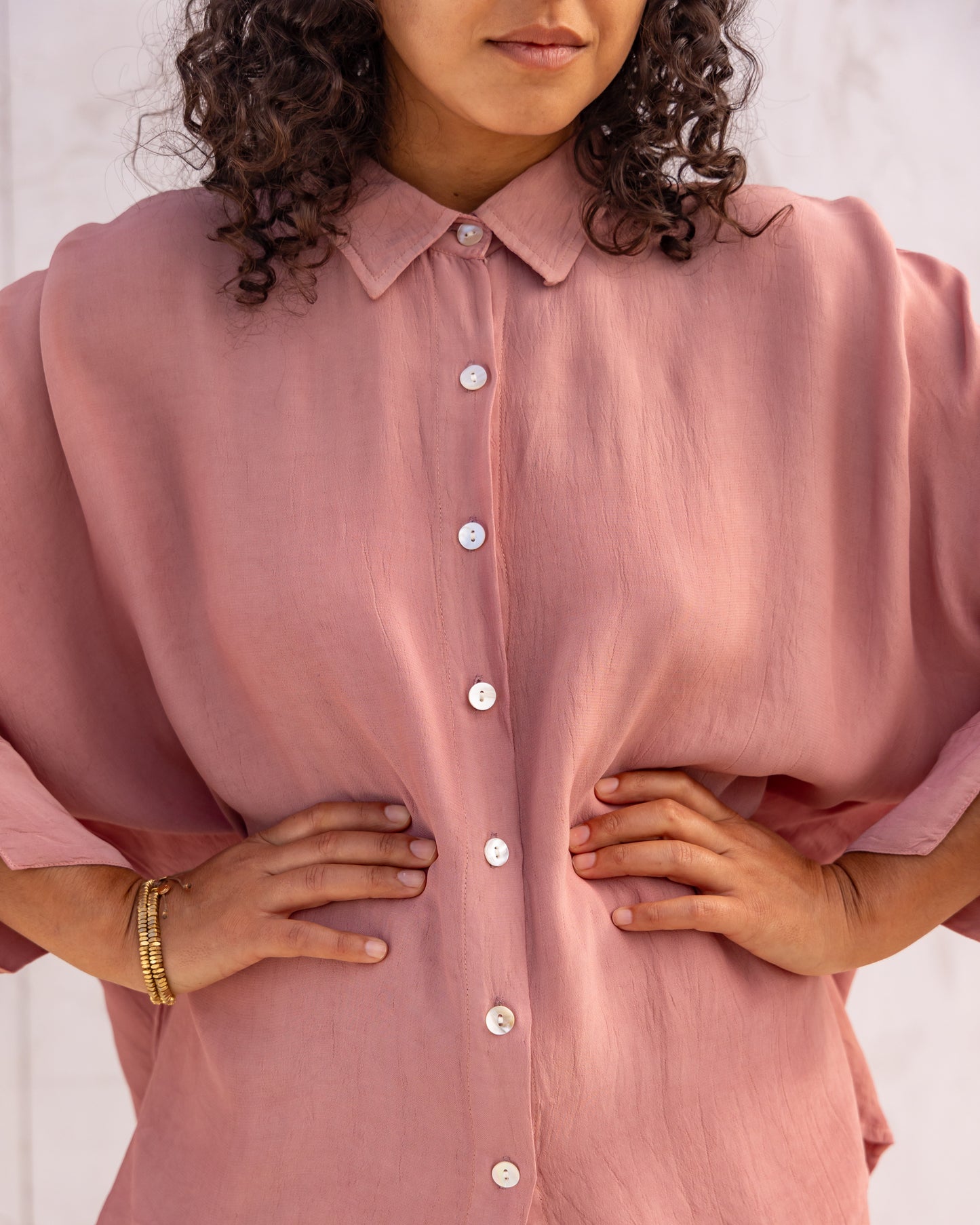 woman dressed in bouviet oversized shirt and miguel straight legged pants in orange peel fibre in dirty rose pink standing in front of a white wall