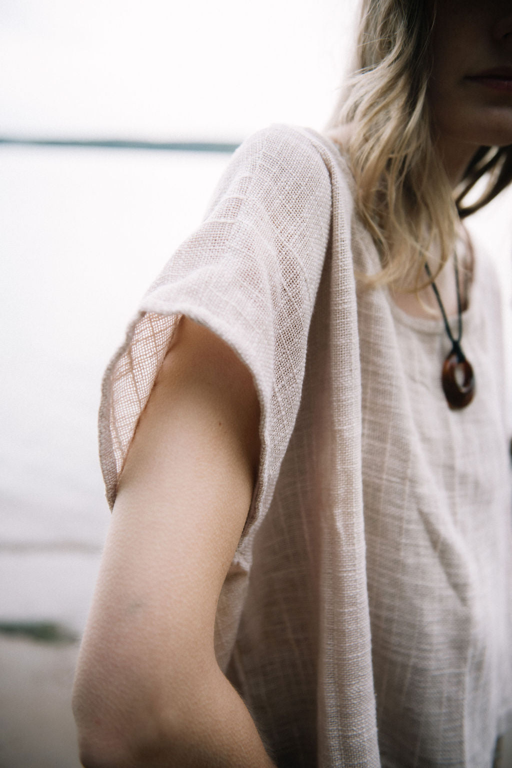 
                  
                    woman dressed in oversized net taupe top in front of ocean
                  
                