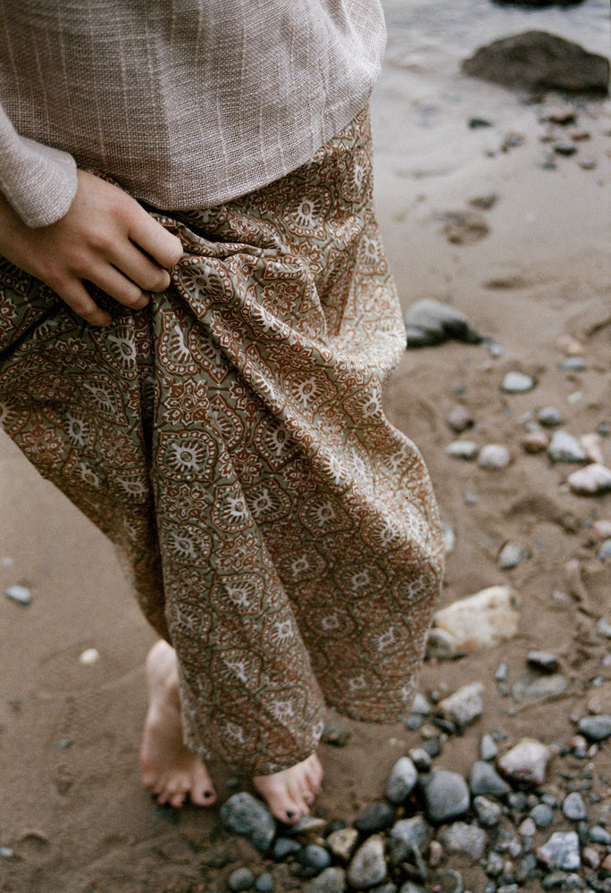 
                  
                    woman dressed in beige patterned mini dress with oversized net taupe top on rocky beach
                  
                