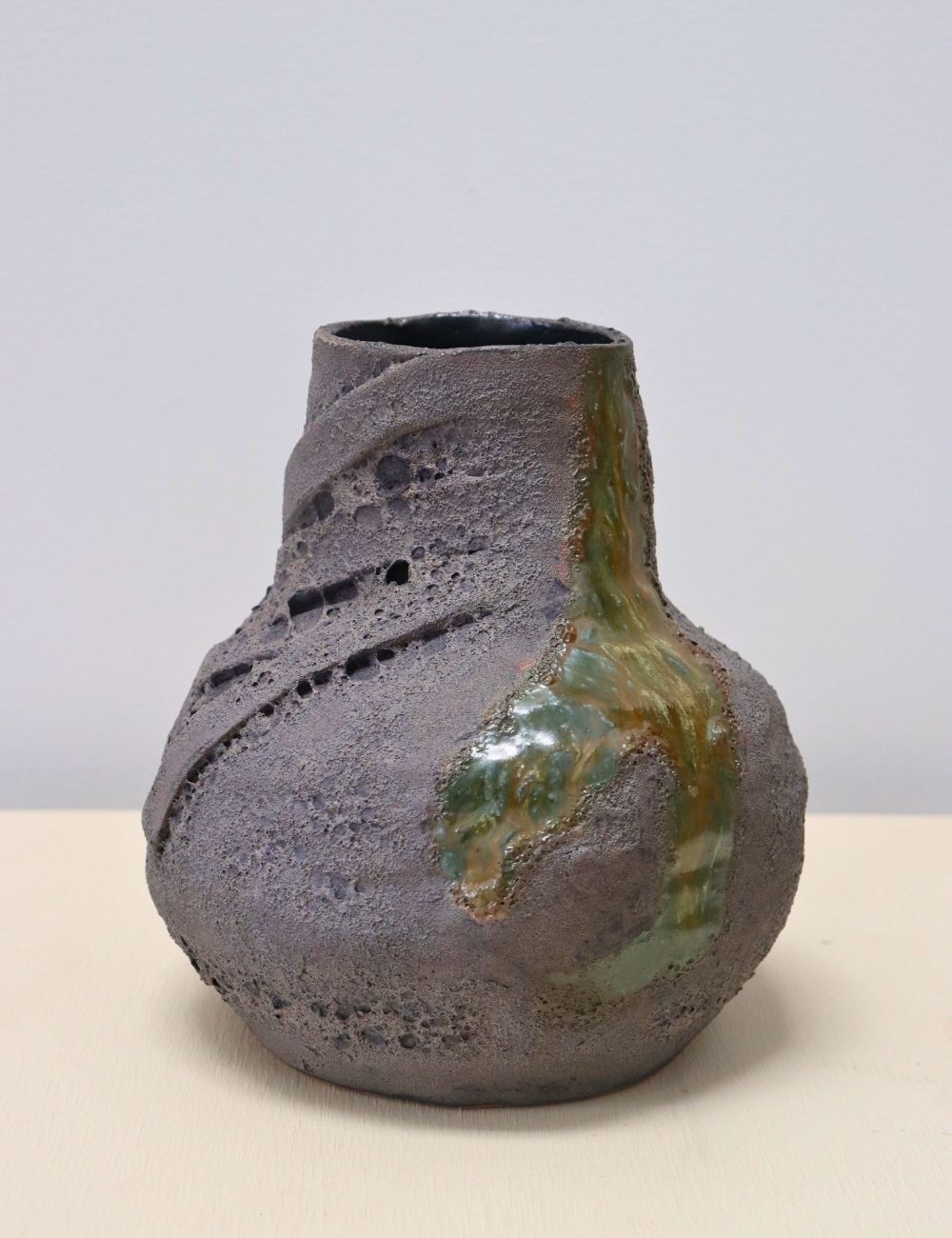 pot with black glaze with volcanic craters in it and a blue green river flowing through it in front of a white wall