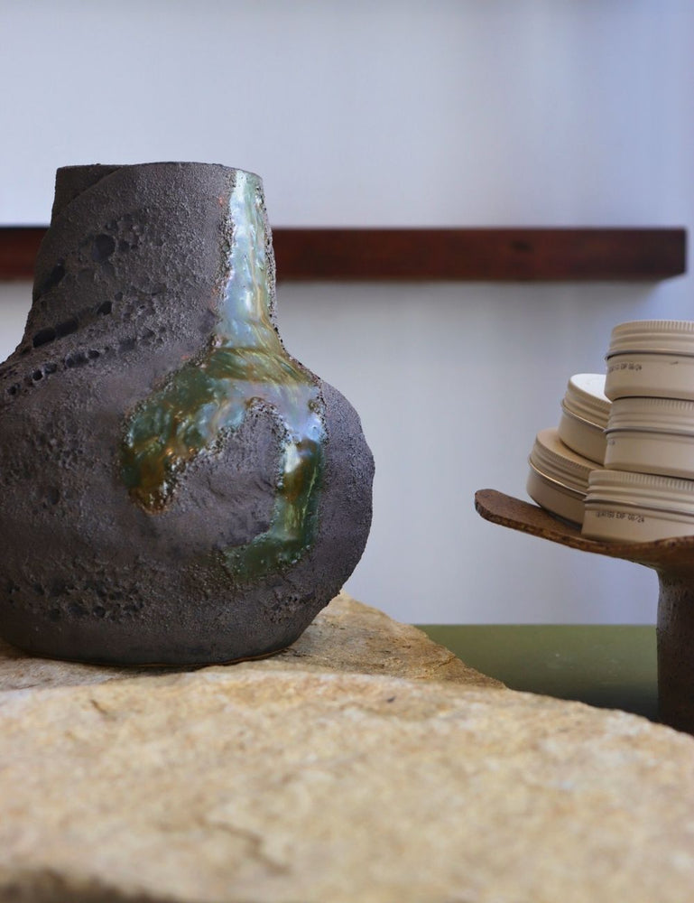 pot with black glaze with volcanic craters in it and a blue green river flowing through it on a stone tile in front of a white wall