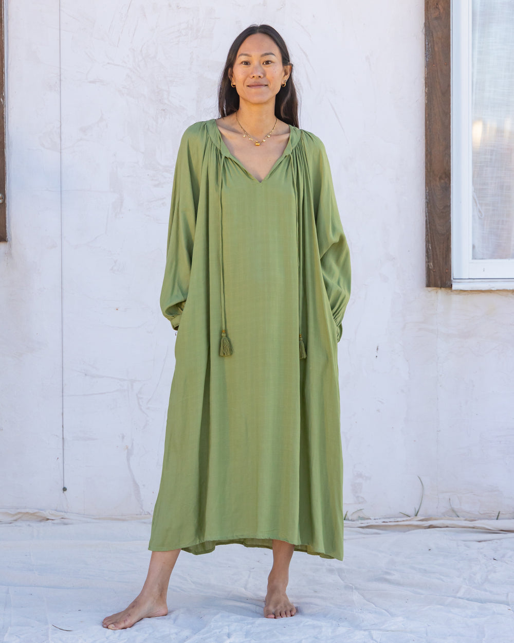 woman dressed in flores organic sugarcane dress in forest green in front of white wall