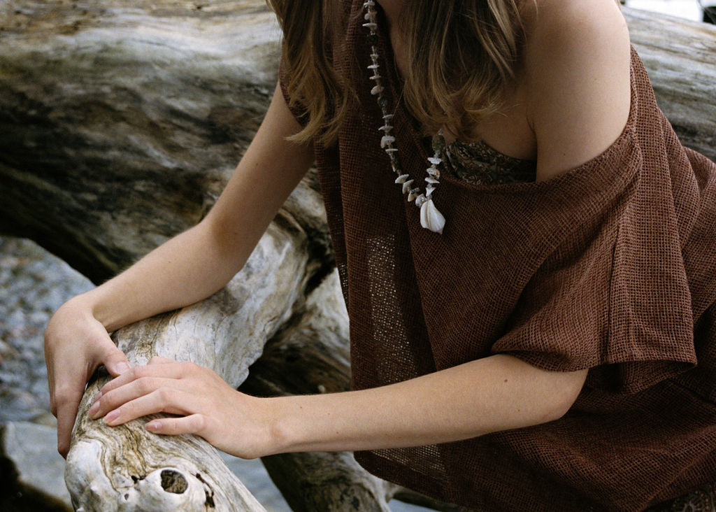 
                  
                    woman dressed in beige patterned midi dress with oversized net rust top in front of drift wood
                  
                