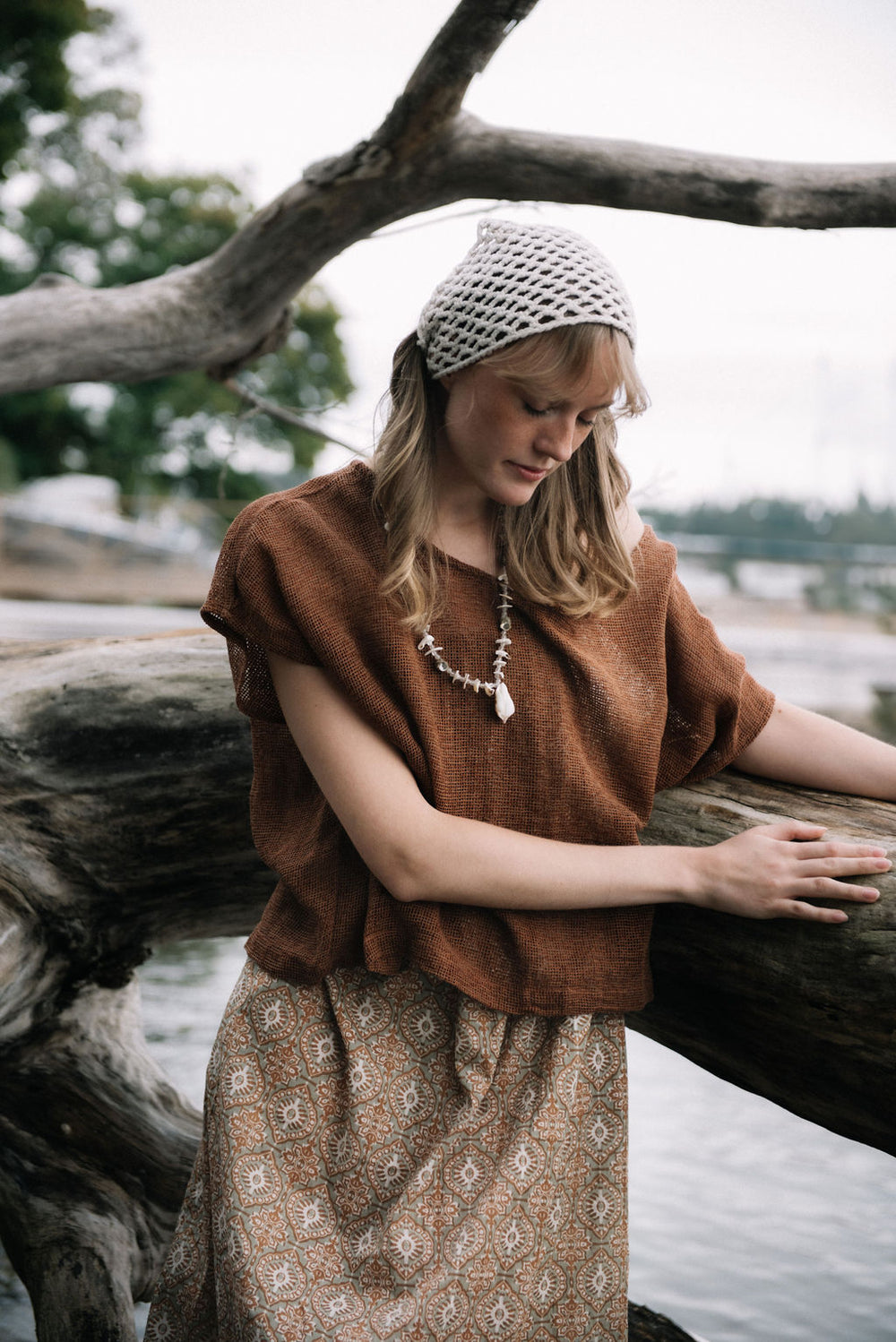 woman dressed in beige patterned mini dress with oversized net rust top in front of drift wood