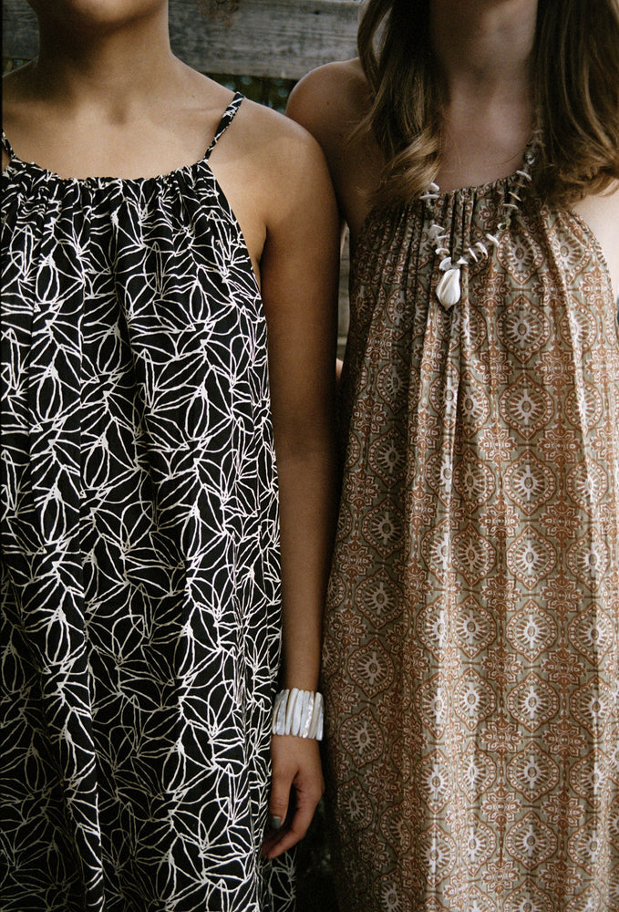 
                  
                    women dressed in beige patterned and black and white patterned midi dresses in front of a fence
                  
                