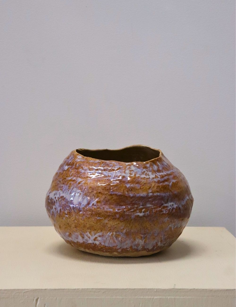 low wonky pot with white and purple glaze in front of a white wall