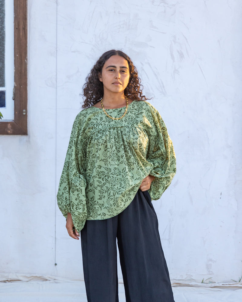 woman dressed in palma billowing sleeves top in gooseberry green print in front of white wall