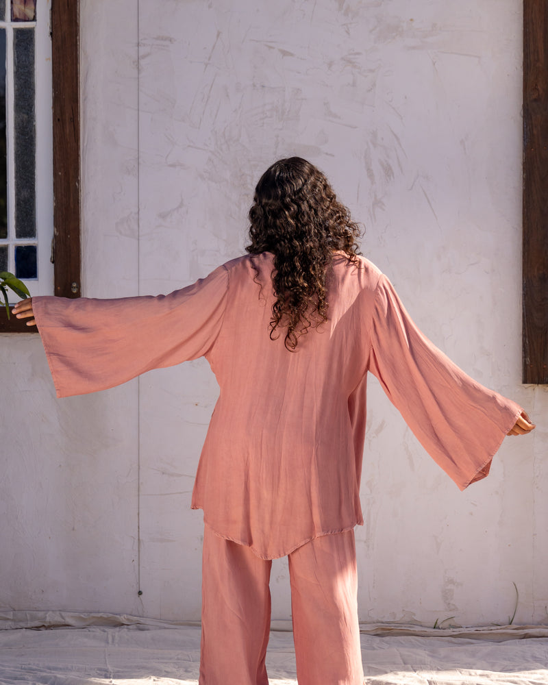 woman dressed in sao wrap top and miguel straight legged pants in orange peel fibre in pink dirty rose standing in front of a white wall