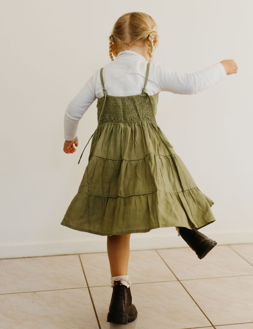 young girl dressed in vincente organic sugarcane tie dress in green forest standing in front of a white wall