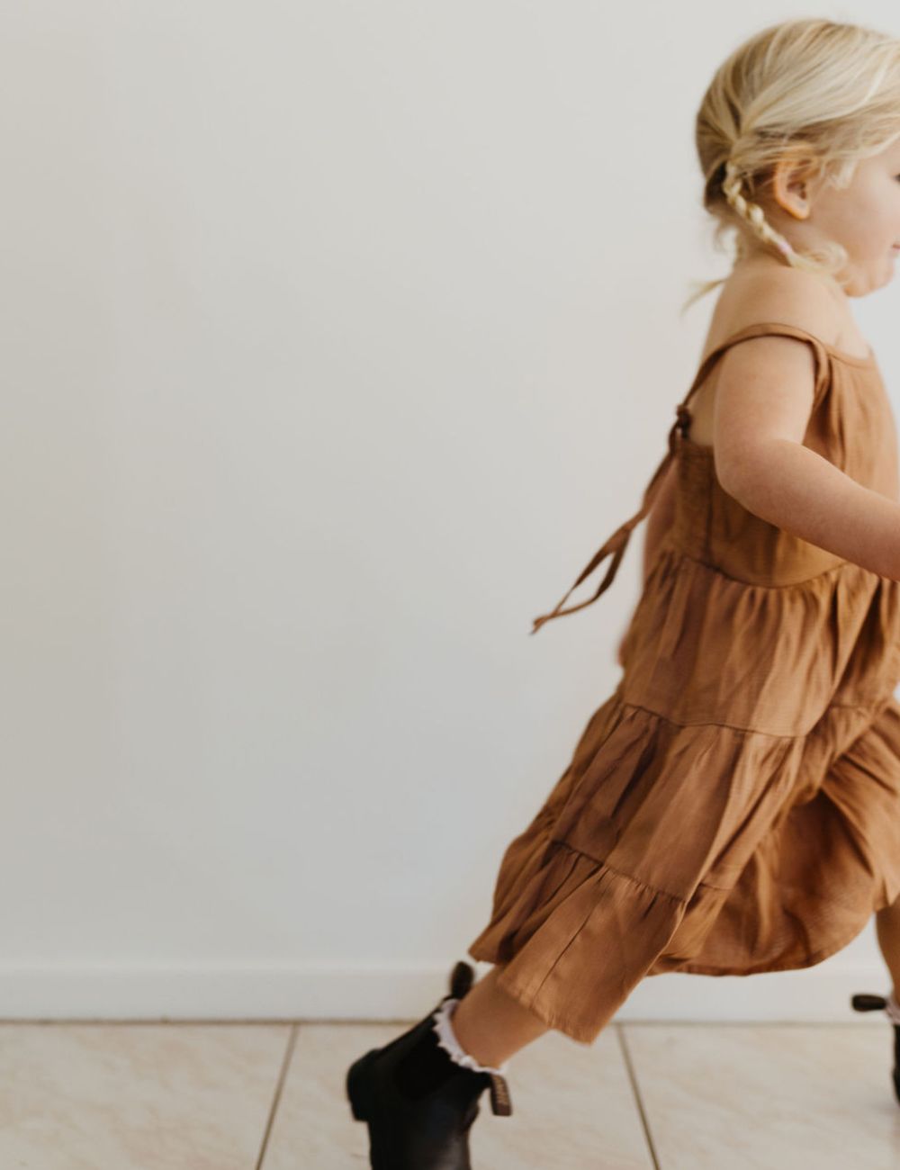 
                  
                    young girl dressed in vincente organic sugarcane tie dress in mulberry standing in front of a white wall
                  
                