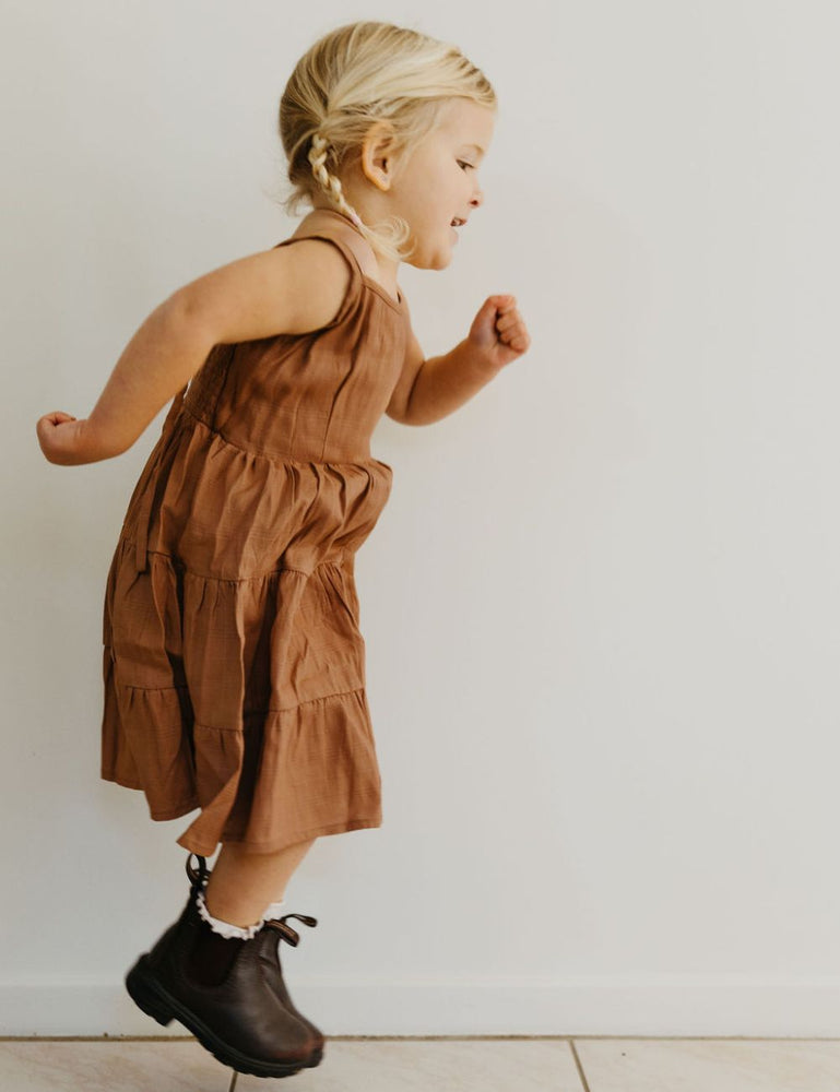 
                  
                    young girl dressed in vincente organic sugarcane tie dress in mulberry standing in front of a white wall
                  
                