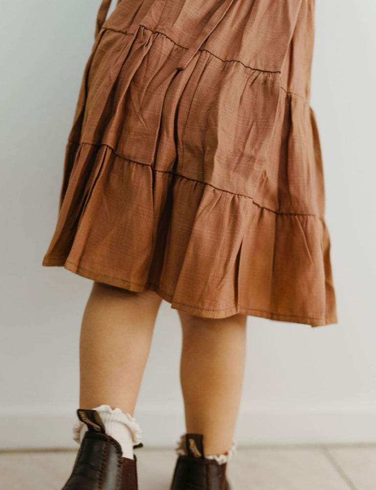 
                  
                    young girl dressed in vincente organic sugarcane tie dress in mulberry standing in front of a white wall
                  
                