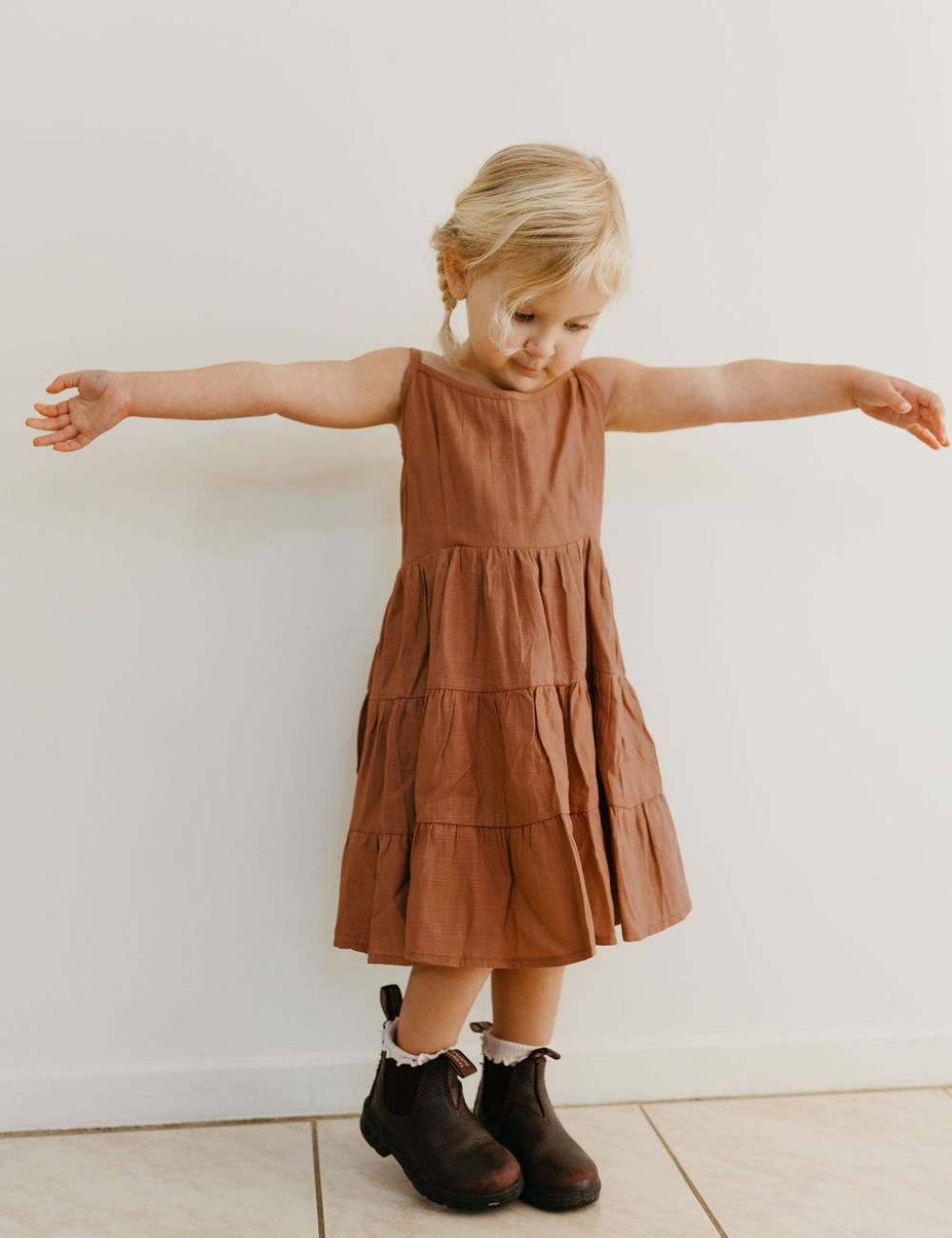 young girl dressed in vincente organic sugarcane tie dress in mulberry standing in front of a white wall